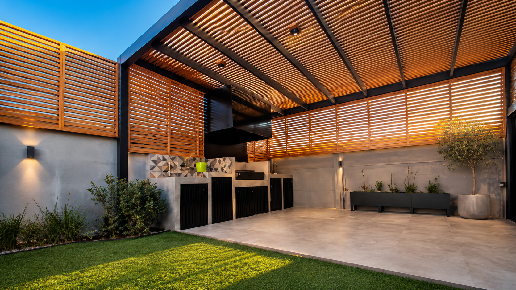Quincho moderno con pérgola de listones de madera, cocina exterior y terraza iluminada al atardecer